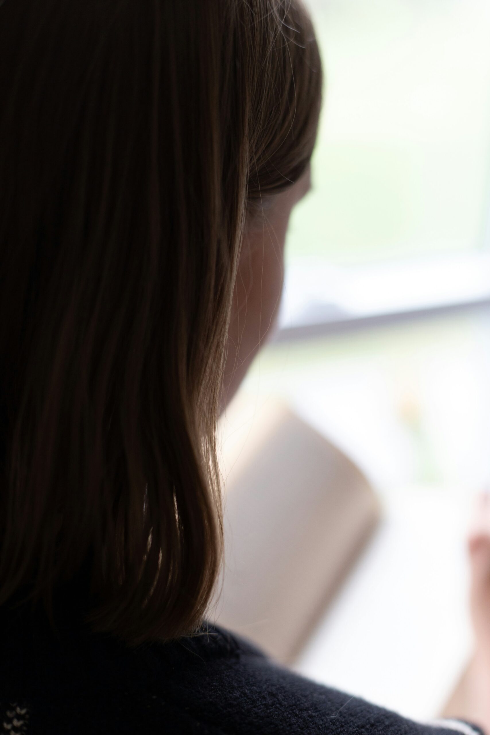 Person with shoulder-length brown hair reading a book near a window.