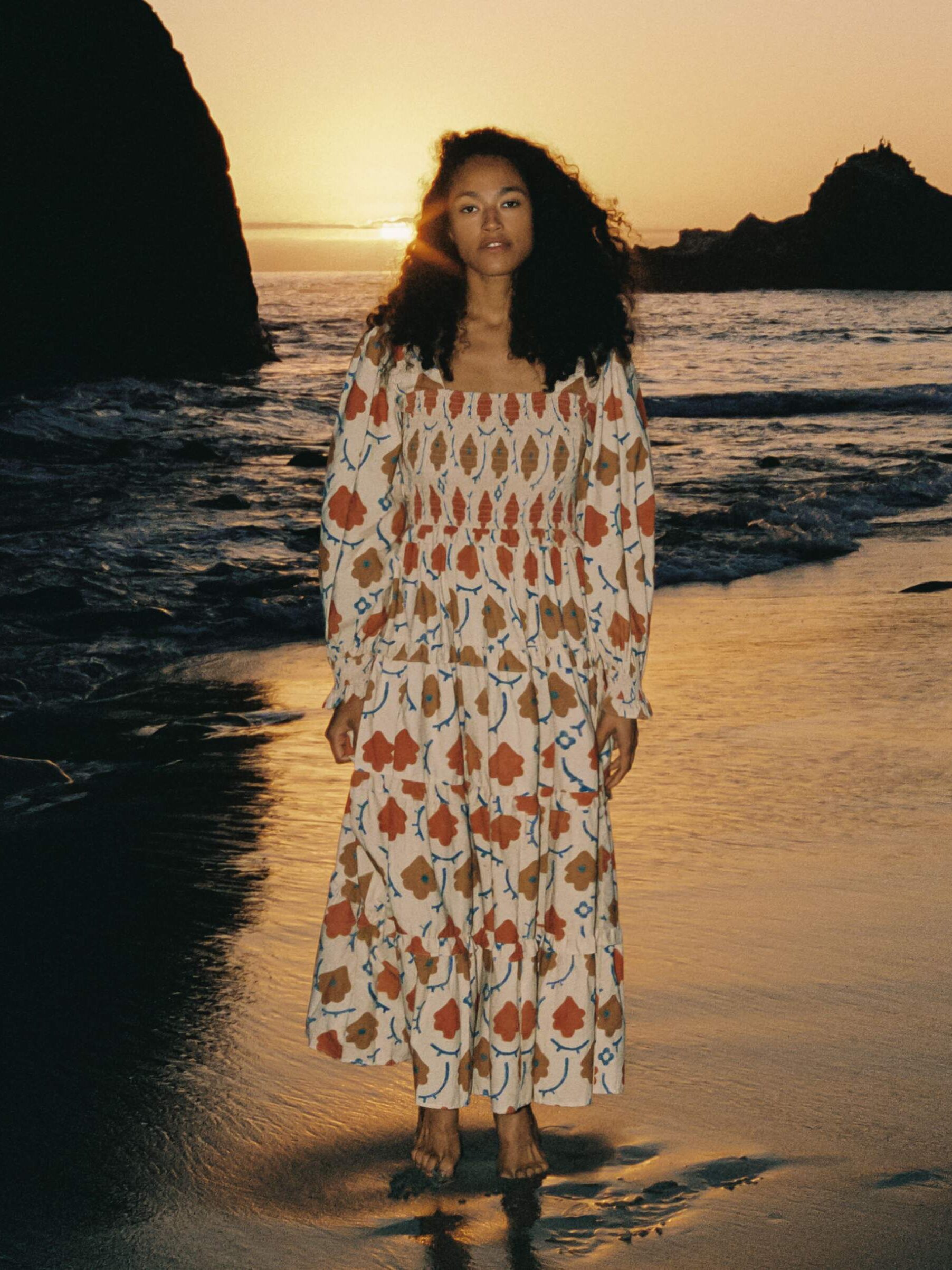 A model on a beach wearing a long sleeve patterned maxi dress from Christy Dawn.