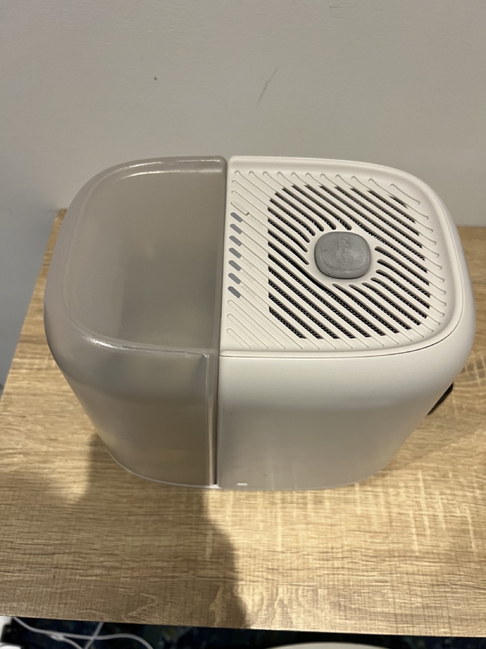 A white and grey dehumidifier sits on a wooden surface, featuring a large vent and control knob on top.