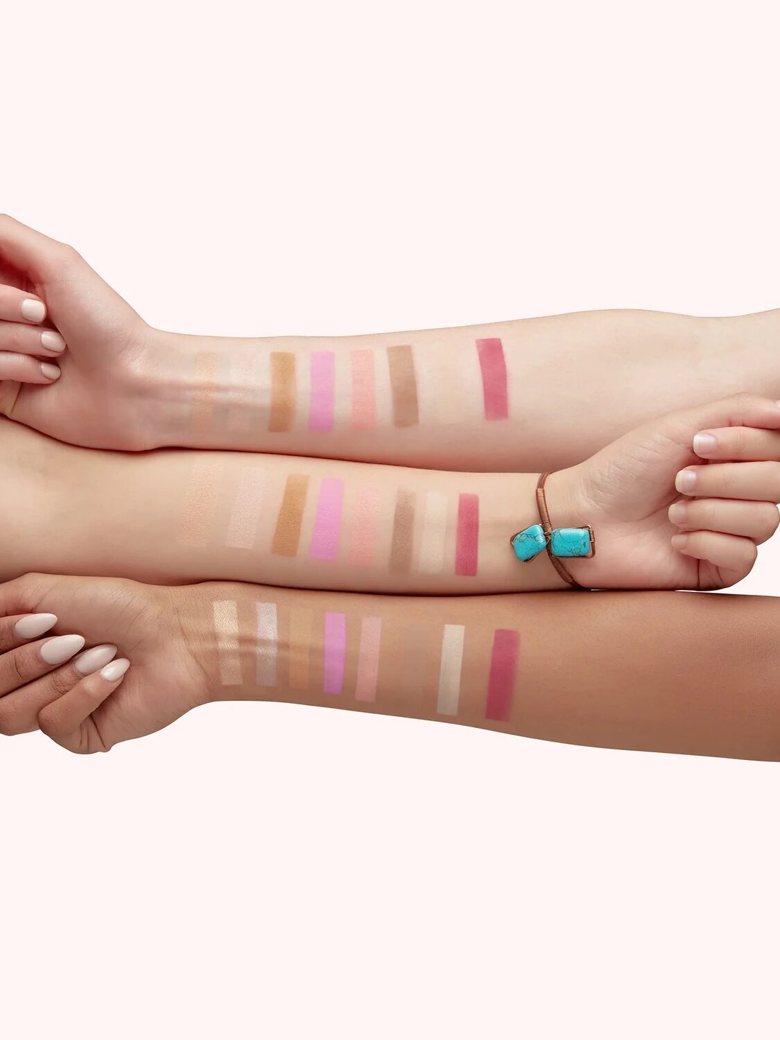 Three forearms with varied skin tones display swatches of makeup products in different shades, showcasing a range of colors from light to dark.
