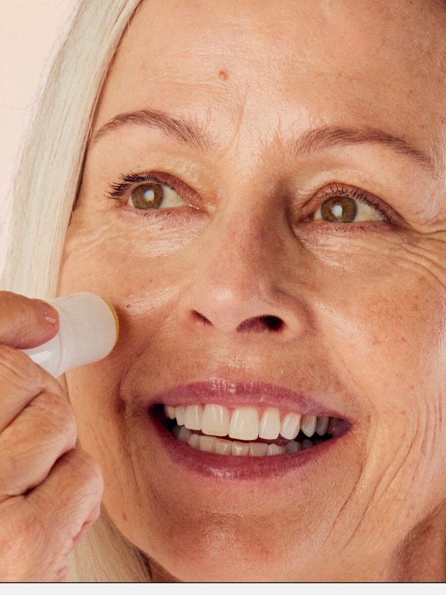 A woman applies a moisture stick to her cheek. Text reads: "Apply for instant moisture on the face and dry body areas, such as lips, hands, elbows, knees, and cuticles.
