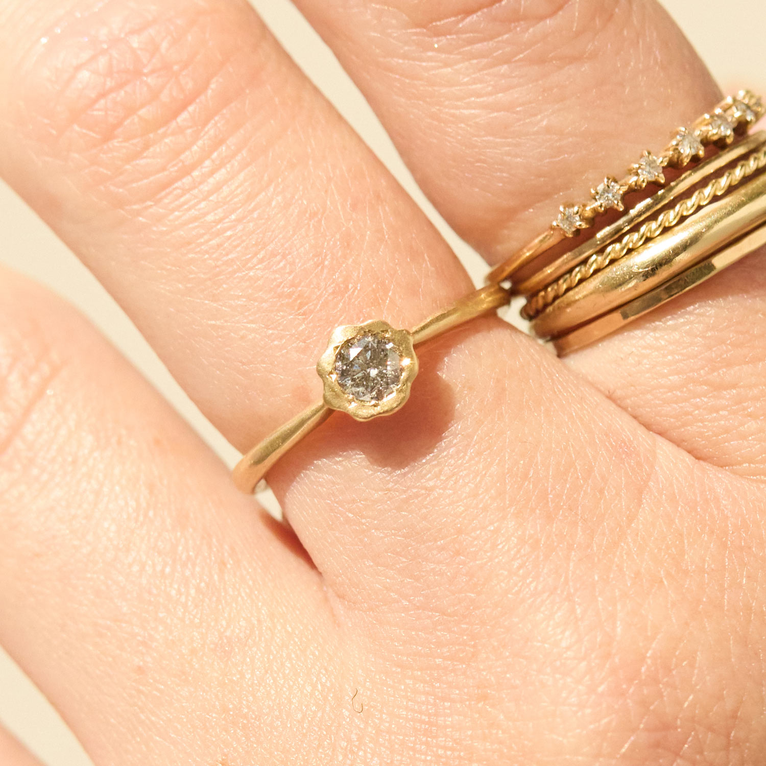 Close-up of a hand wearing three gold rings, one with a rough-cut stone and two with small diamonds and detailed bands.