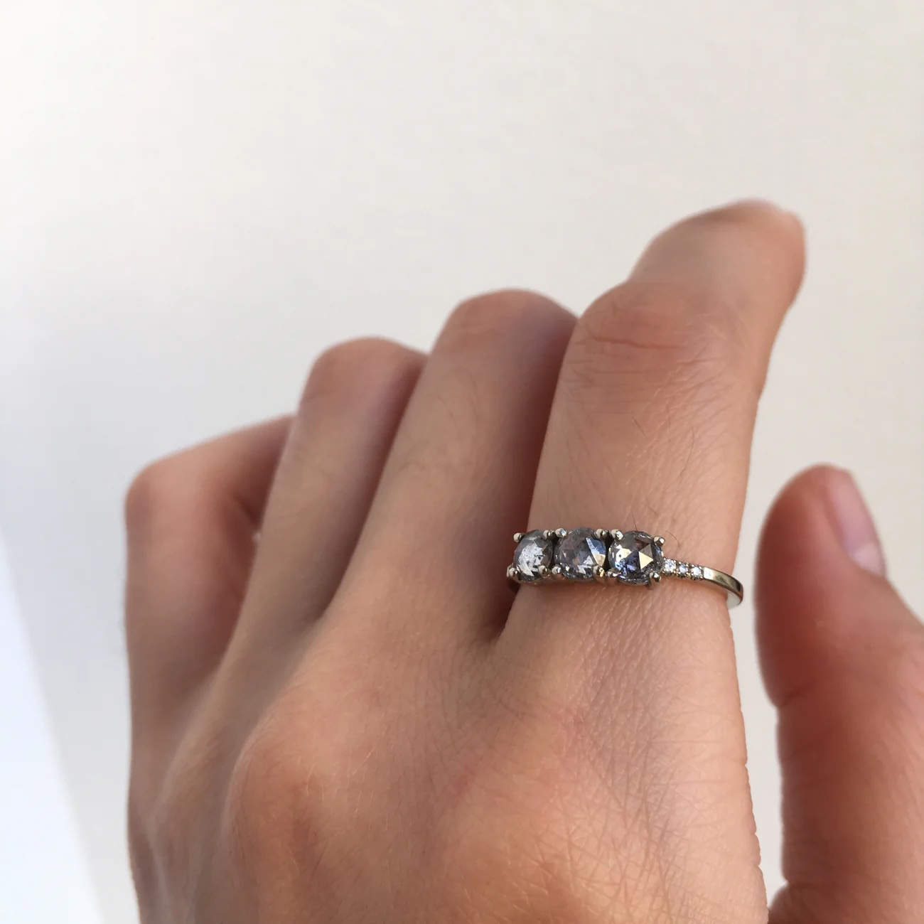 A hand wearing a silver ring with three large stones and smaller stones on the band, shown against a plain light background.