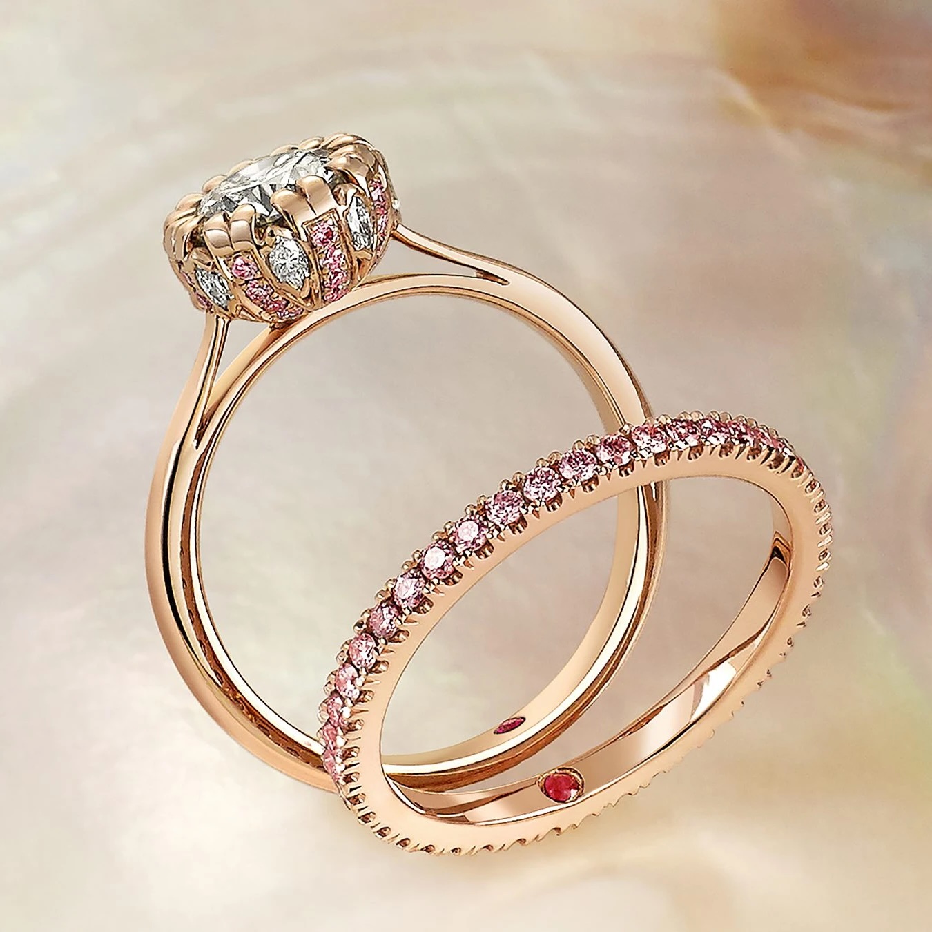 Two rose gold rings: one with a large central diamond surrounded by smaller stones, and one eternity band set with pink gemstones, displayed on a pearlescent background.