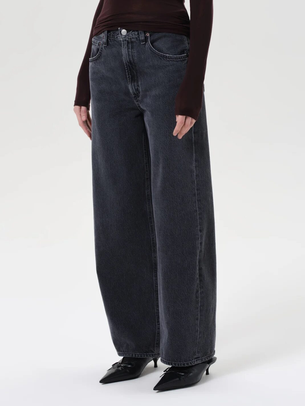 Person wearing wide-leg, faded black jeans with a high waist and black pointed-toe shoes, standing against a plain light background.