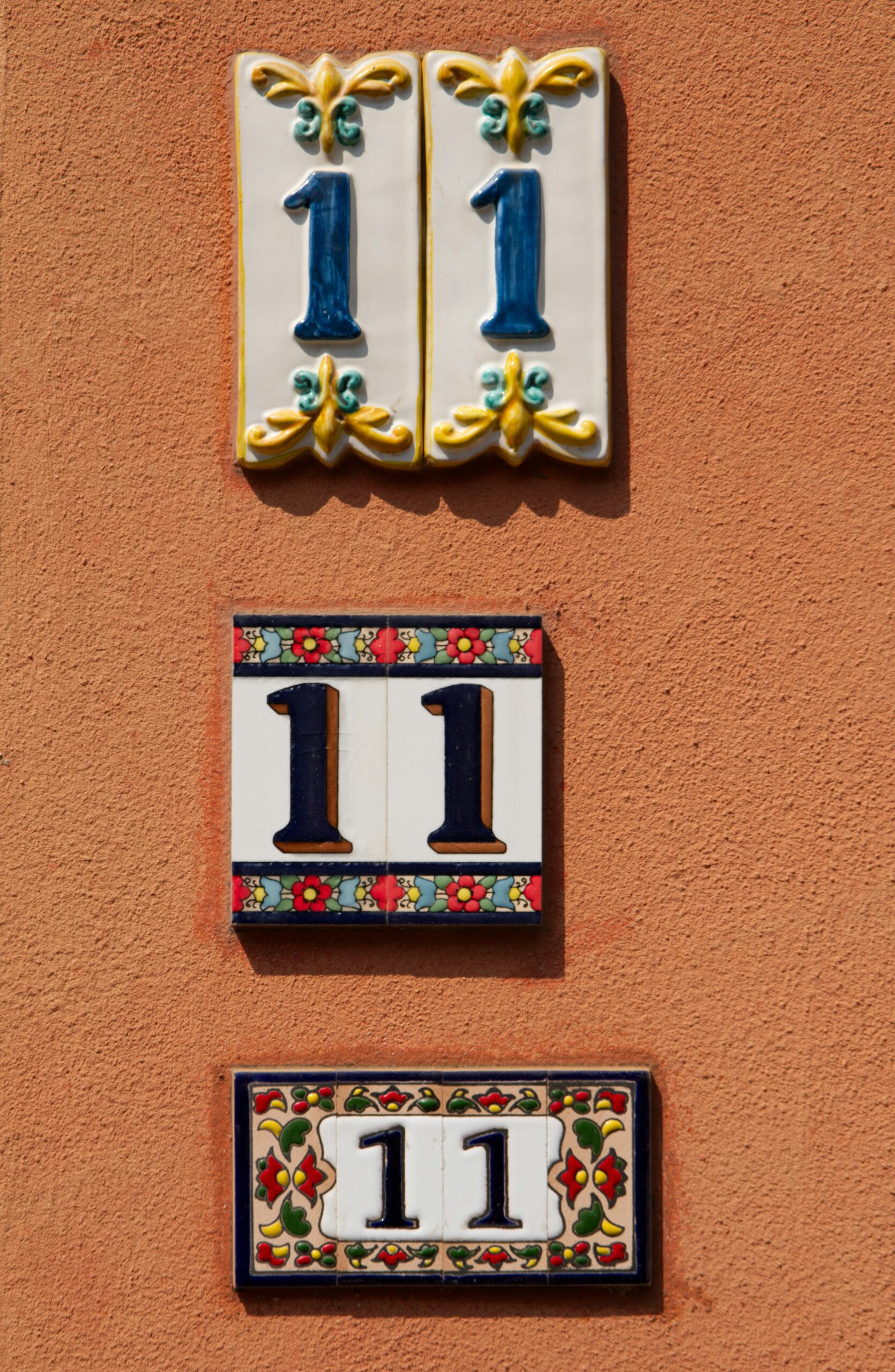 Three decorative ceramic tiles, each displaying the number sequence 11, are mounted on a textured orange wall.