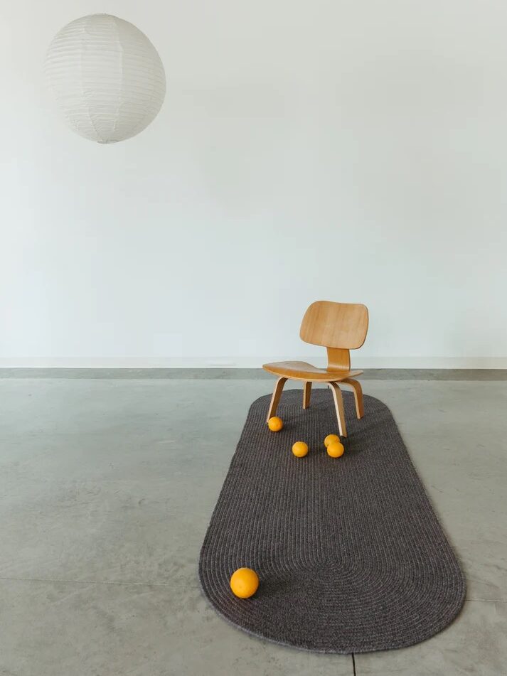 A wooden chair sits on a gray rug with six orange balls scattered around it; a white paper lantern hangs above against a plain white wall.
