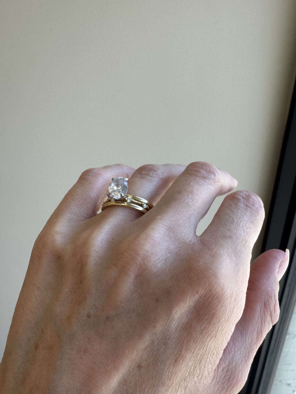A hand wearing a gold ring with a large oval-shaped clear gemstone, set against a neutral background.