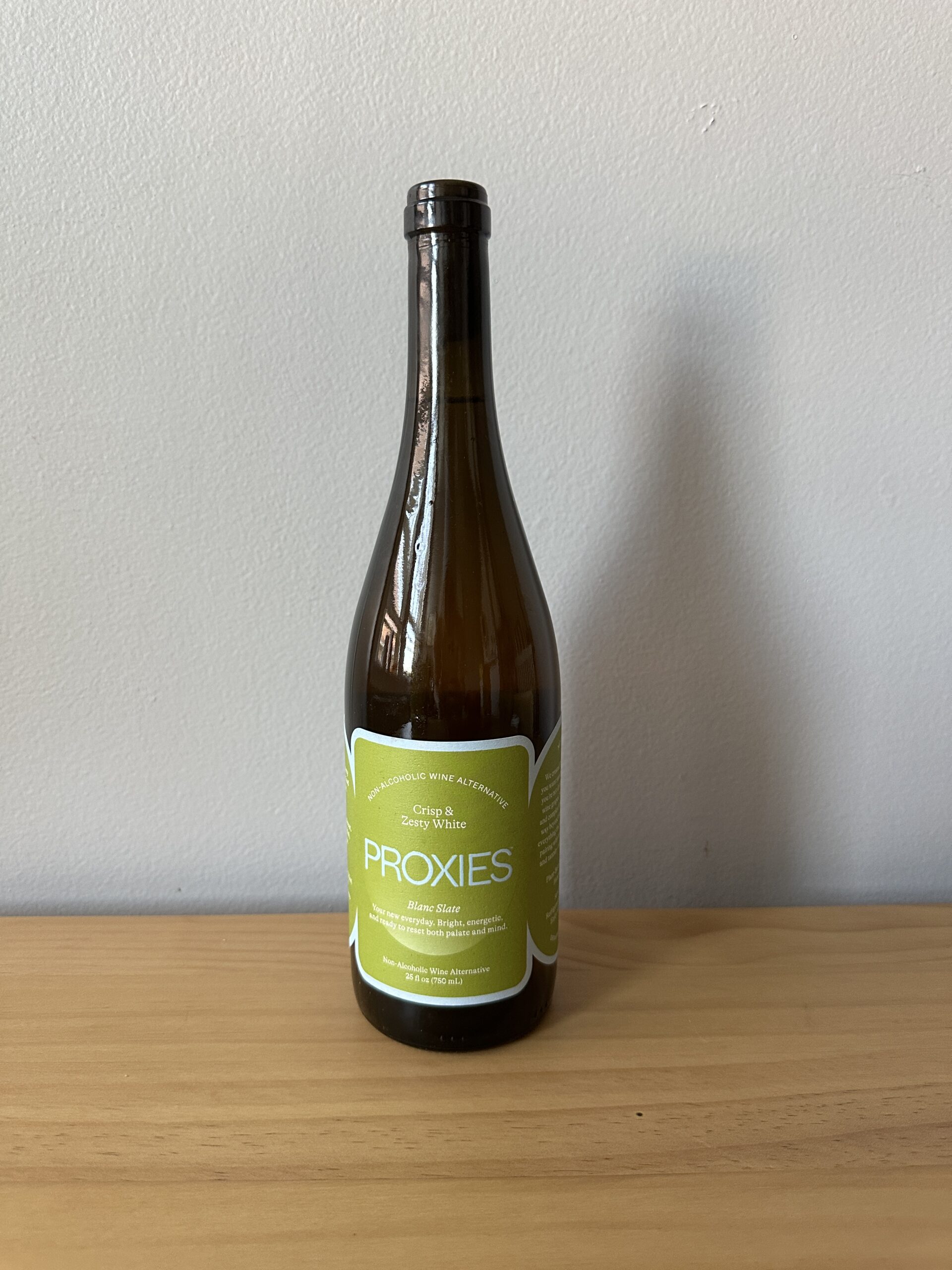 A brown glass bottle labeled "Proxies" with a green and white label, placed on a wooden surface against a plain light-colored wall.