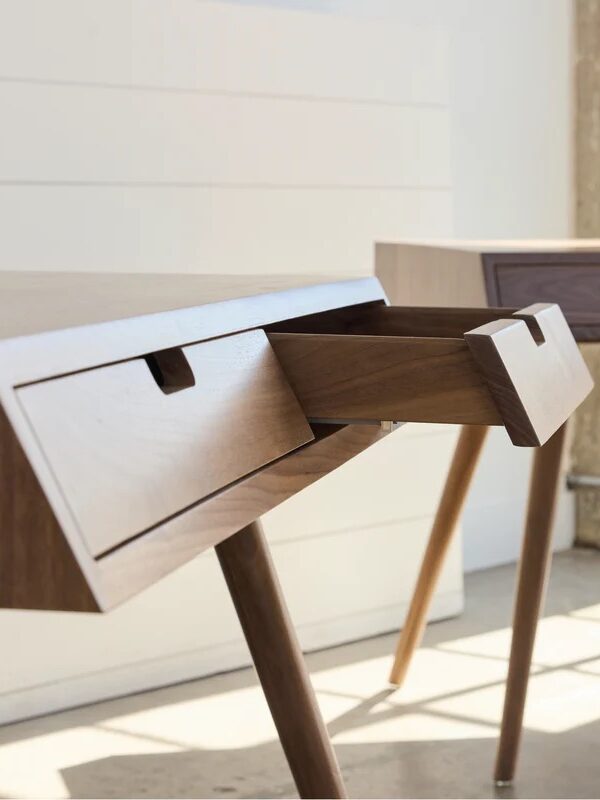 Wooden desks with open drawers and angled legs, set in a sunlit room.