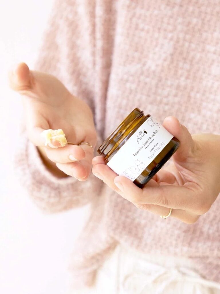 A hand dipped into a jar of 100% Pure's Body Butter.