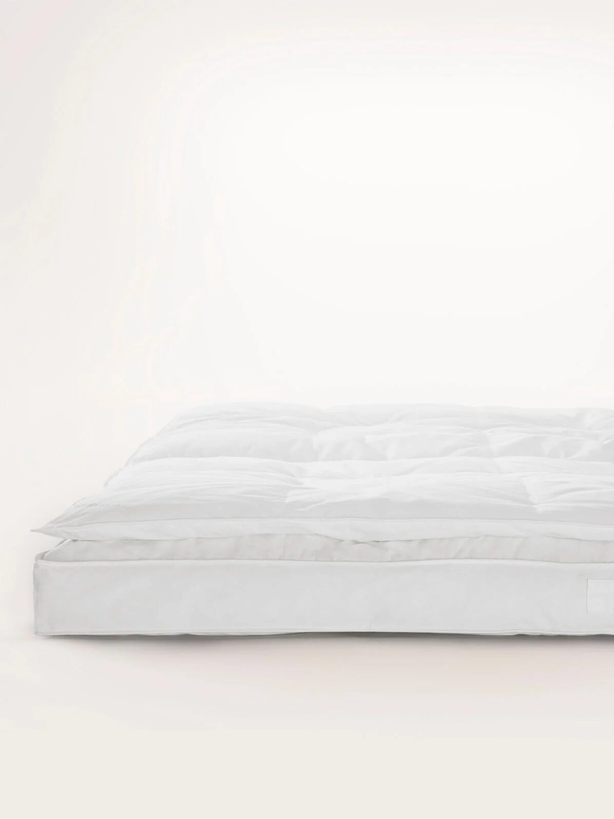A white mattress topper on a white background. The topper has a quilted pattern and visible padding.