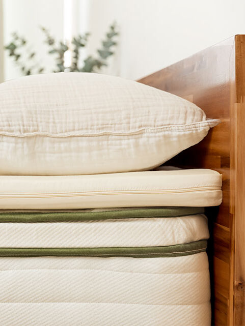 Pillow and textured beige blanket on a neatly made bed with a light-colored mattress in a well-lit bedroom.