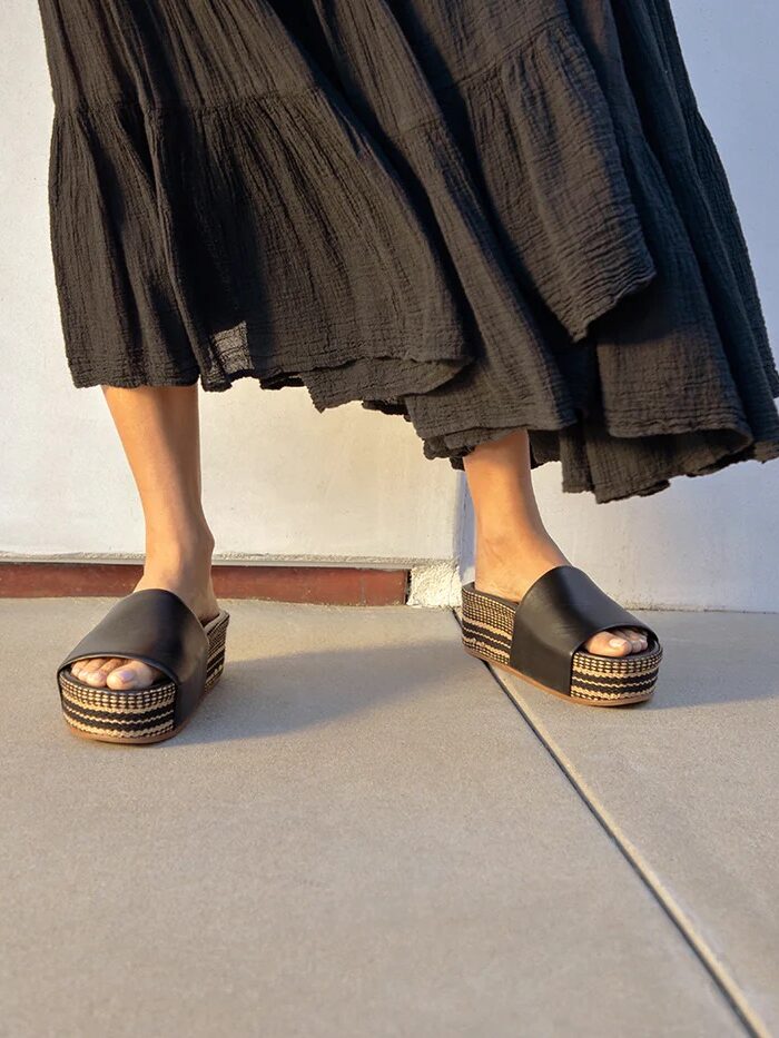 A person wearing a long black skirt and black platform sandals stands on a smooth outdoor surface.