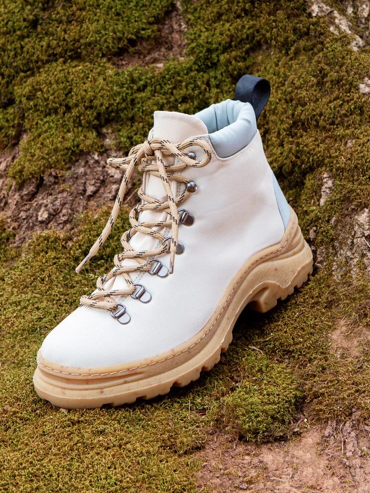 A white hiking boot with tan laces and a rugged sole rests on mossy ground.