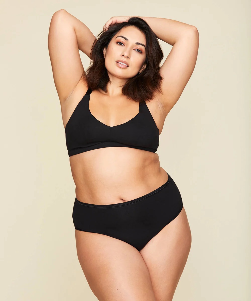 Person wearing a black bikini poses with one hand on head and the other on hip against a plain background.