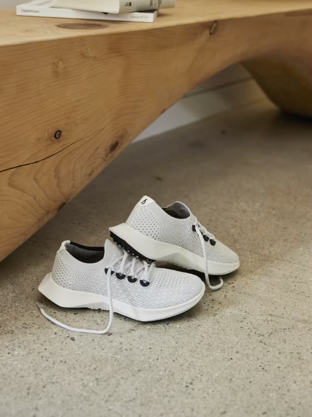 White athletic shoes with black accents are placed on a gray concrete floor next to a wooden bench.