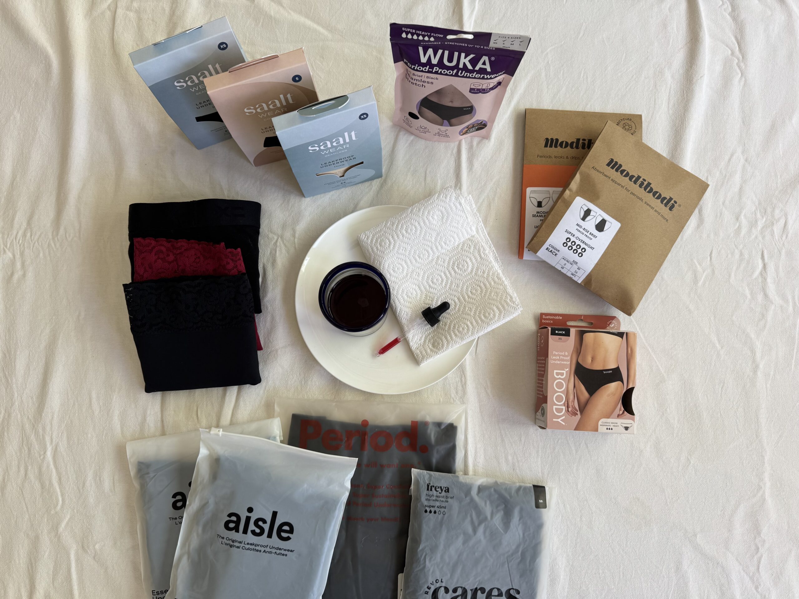 A collection of menstrual products including period panties, menstrual cups, and their packaging are displayed on a white surface.
