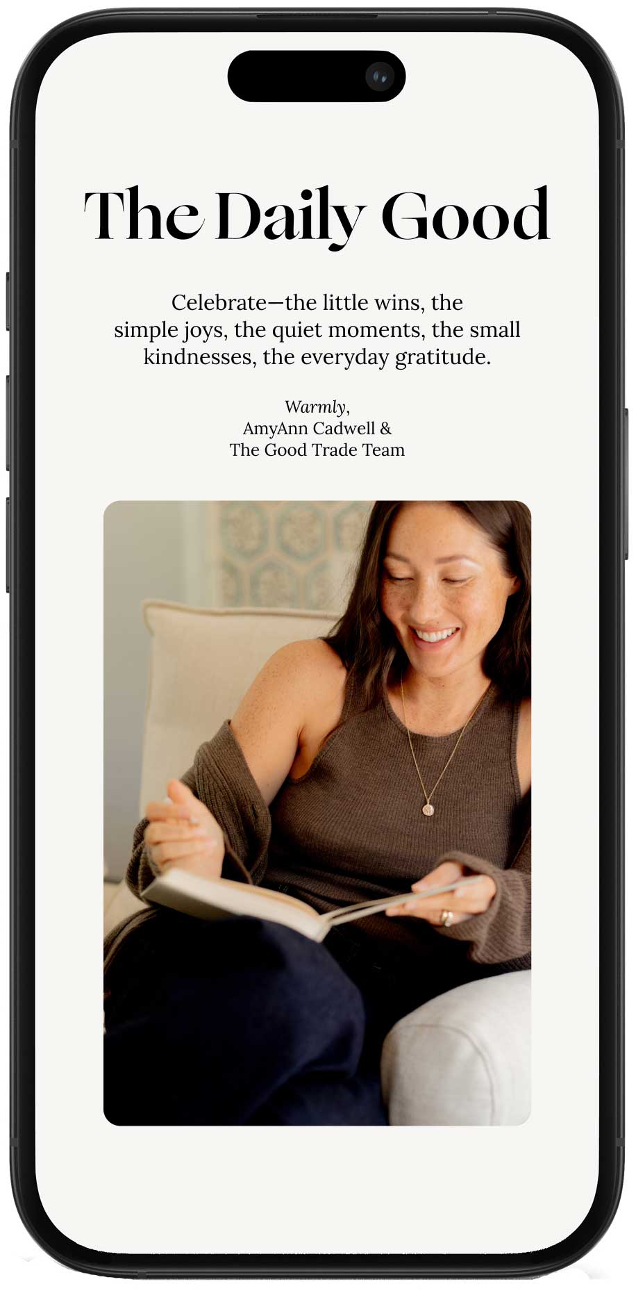 A woman sits on a couch smiling while reading a book, featured on a phone screen displaying a message from "The Daily Good.