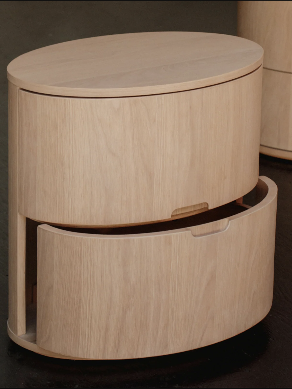 Wooden oval-shaped storage unit with two compartments; the top compartment has a lid and the bottom one is a slide-out drawer.