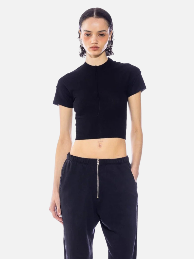 Person wearing a black crop top and black pants with a zipper, standing against a plain white background.