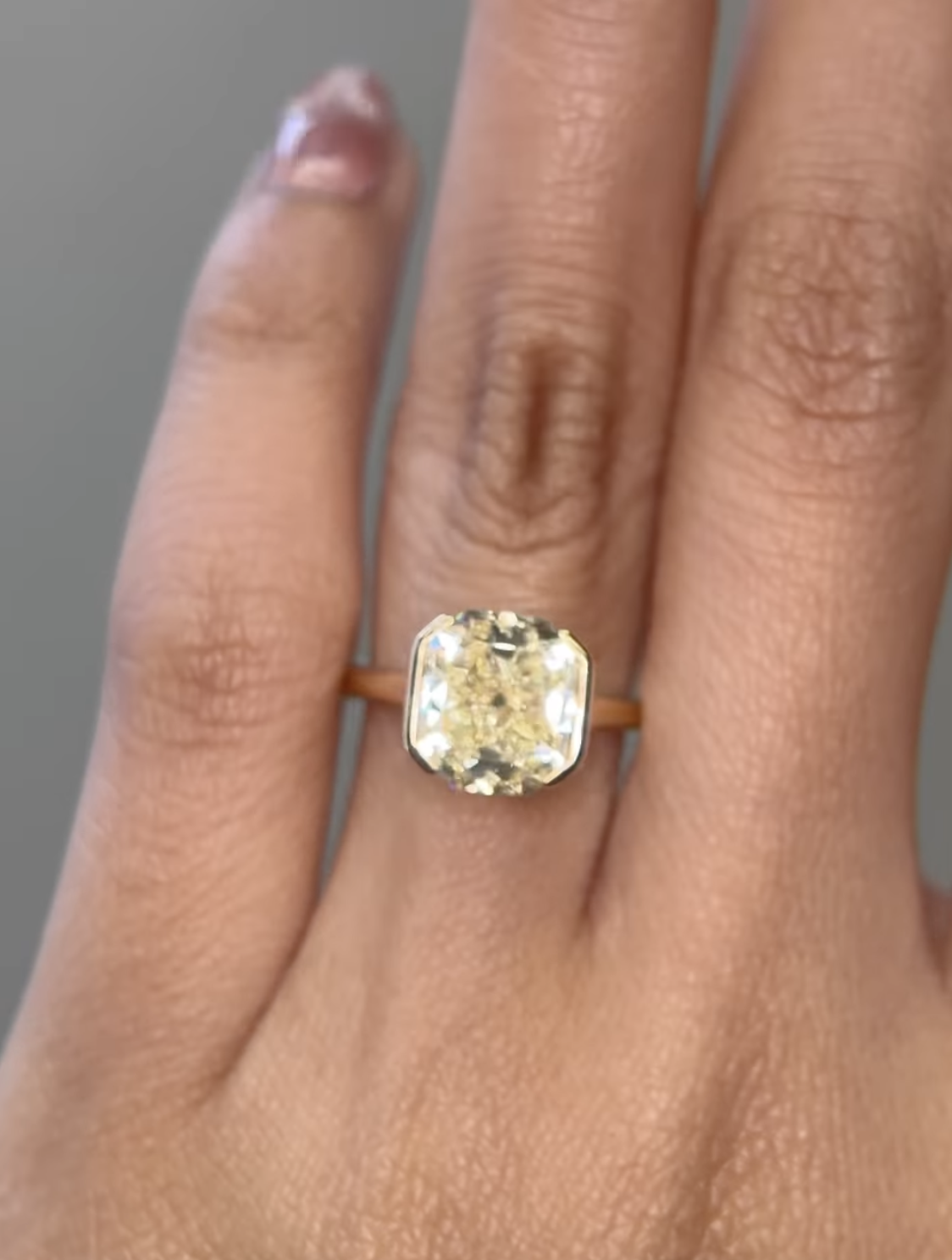 A hand wearing a gold band ring with a large, cushion-cut yellowish diamond set in a bezel setting.