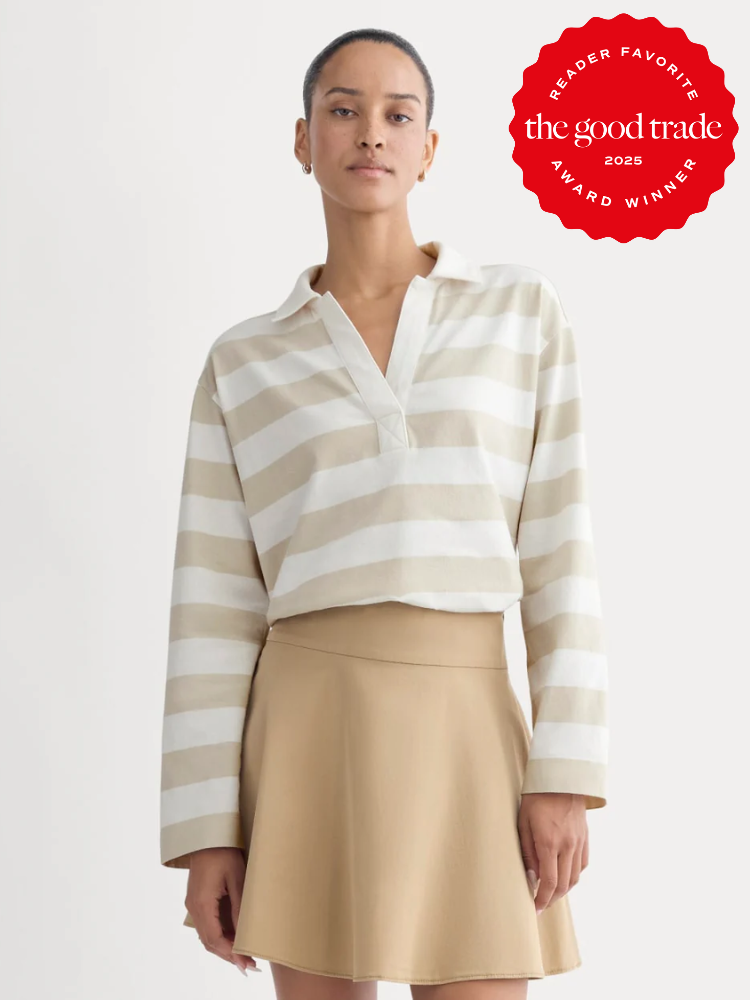 Woman wearing a beige and white striped long-sleeve shirt and a tan skirt stands against a plain background. A red "The Good Trade 2025 Award Winner" badge appears in the top right corner.