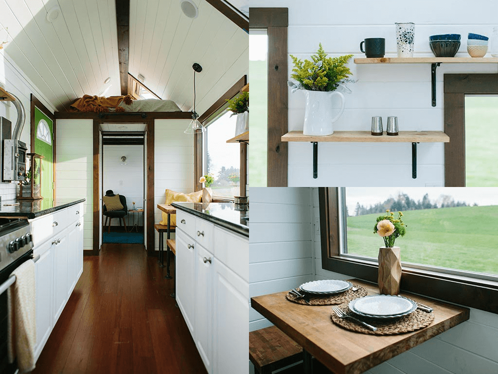 Interior of a tiny house featuring a kitchen with white cabinets, open shelving with decor, a small dining nook with two place settings, and a loft bed in the background.