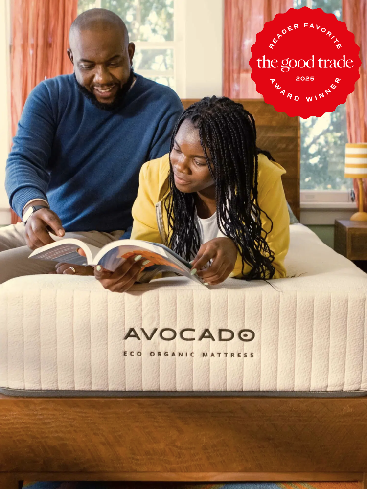 A man and woman sit on an Avocado Eco Organic Mattress, reading a book together. There's a red badge indicating "The Good Trade 2025 Reader Favorite Award Winner" on the top right.