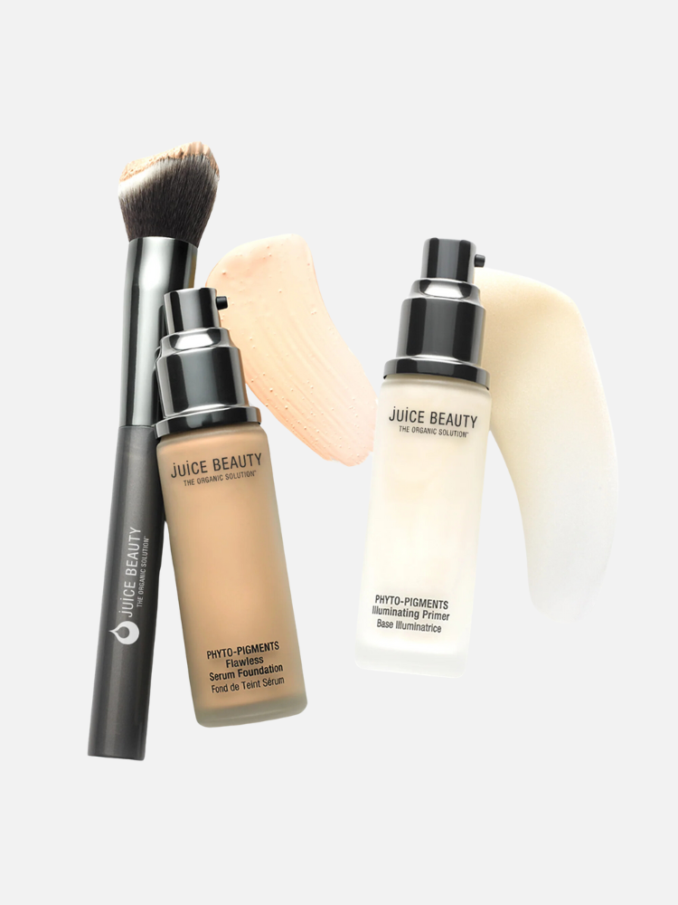 Two Juice Beauty products, a serum foundation and an illuminating primer, are arranged with a black makeup brush against a neutral background. Samples of the foundation and primer are swiped beside them.