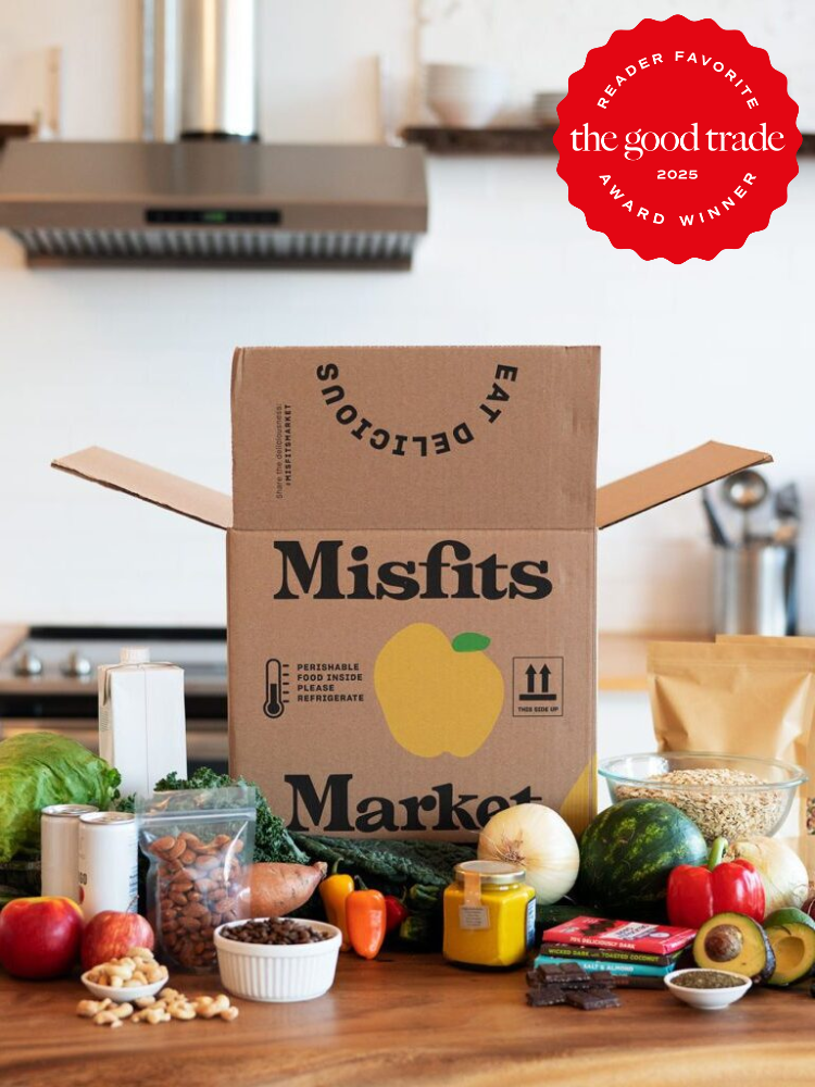 An open Misfits Market box on a kitchen counter surrounded by assorted fruits, vegetables, and packaged goods. A red award badge is displayed in the top right corner.