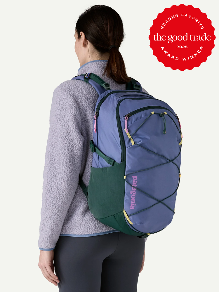 A woman wearing a light purple fleece jacket has a blue and green Patagonia backpack on her back. A red "The Good Trade Reader Favorite 2025 Award Winner" badge is in the upper right corner.