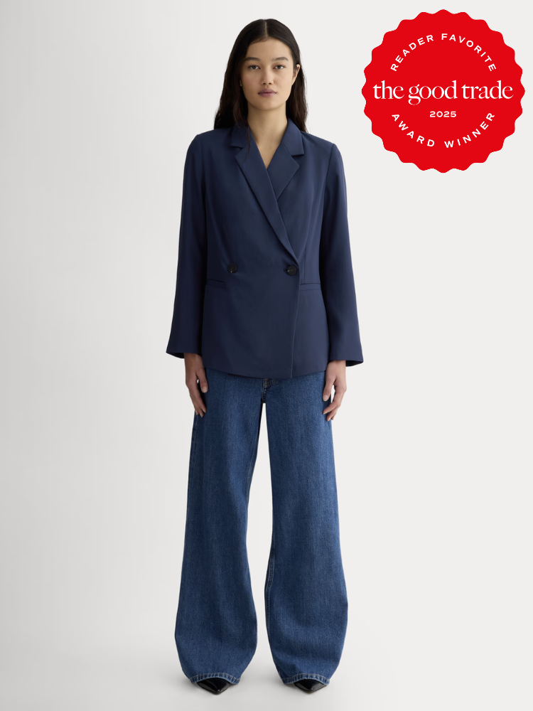 A woman stands facing forward wearing a navy blazer and wide-leg blue jeans. A red "The Good Trade 2025 Award Winner" badge is displayed in the top right corner.