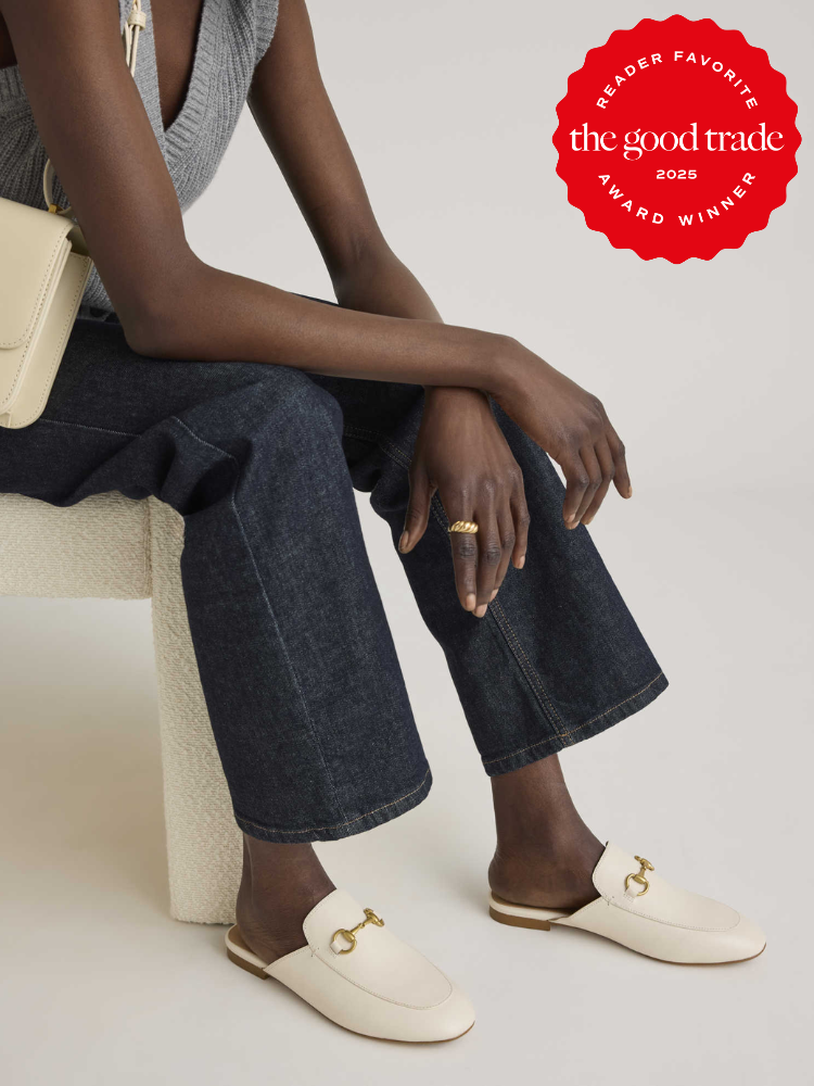 Person sitting on a chair wearing a gray top, dark jeans, and white loafers with gold accents. A cream-colored purse is on their shoulder. A red award badge is displayed in the top right corner.