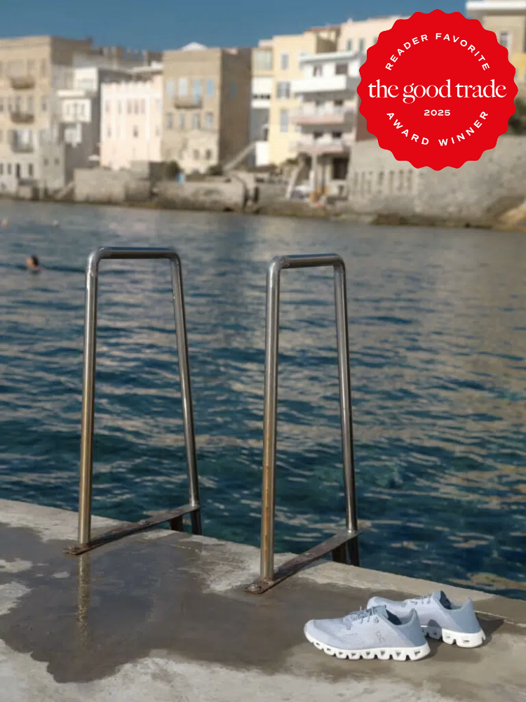 A ladder leads into the sea with a pair of sustainable sneakers on the concrete. Buildings line the shoreline in the background. An award badge is in the top right corner.
