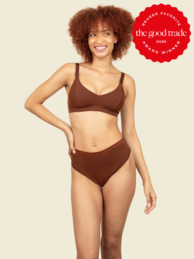 Person wearing brown underwear set, standing and smiling, with "The Good Trade Award Winner 2025" badge in the corner.