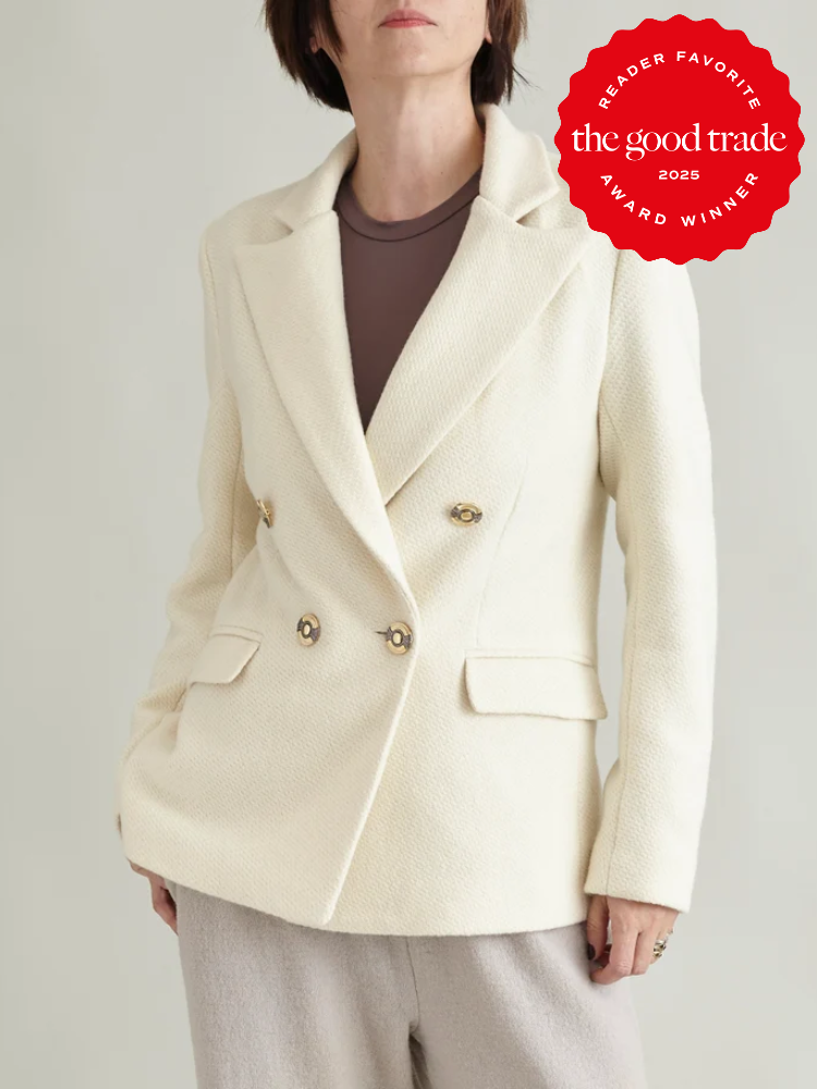 Person wearing a cream-colored double-breasted blazer and beige pants, with a red award badge in the corner.