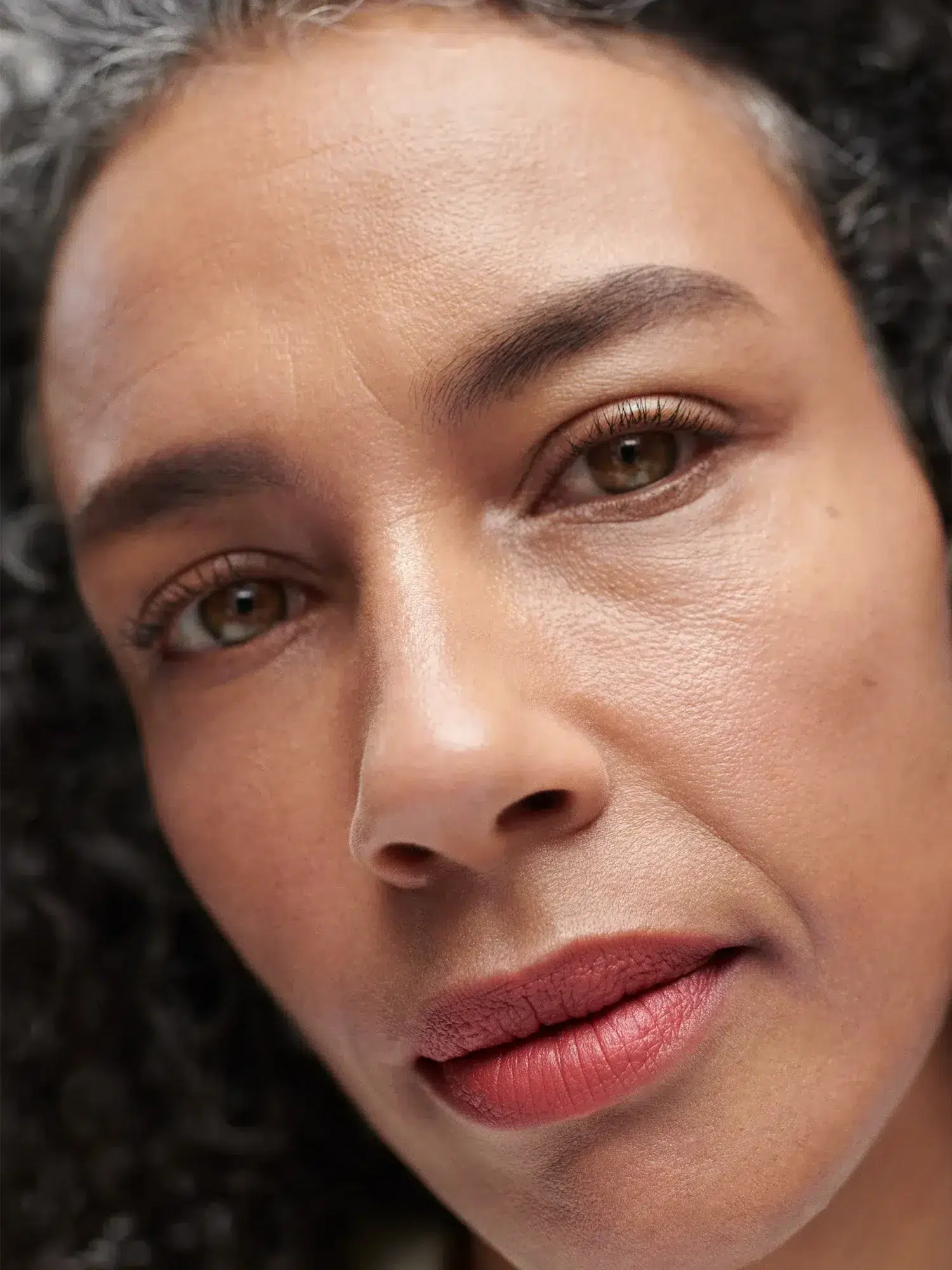 Close-up of a person with curly hair, looking directly at the camera with a neutral expression.